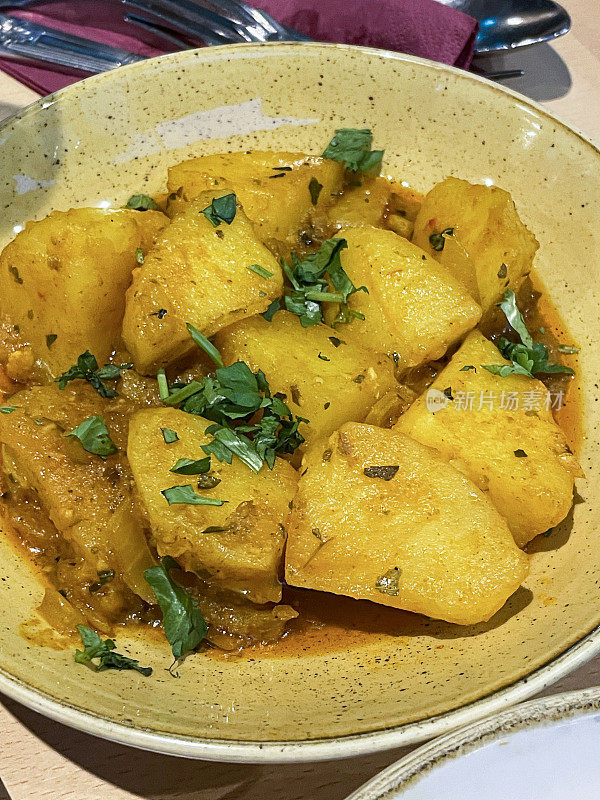 餐厅设置的特写图片，盘子里有孟买aloo(切块的土豆)，用香料调味，孜然，咖喱，大蒜，garam masala，姜黄，芥末籽，辣椒粉，盐和胡椒，桌面背景，升高的视图